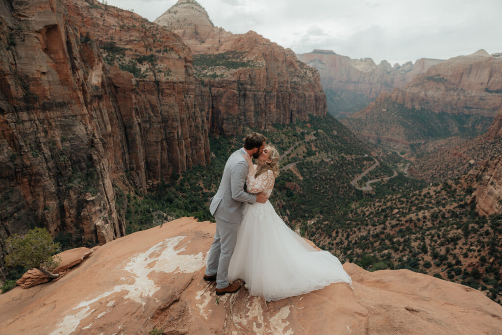 Bride and groom kiss on a cliff edge above a canyon in Zion National Park