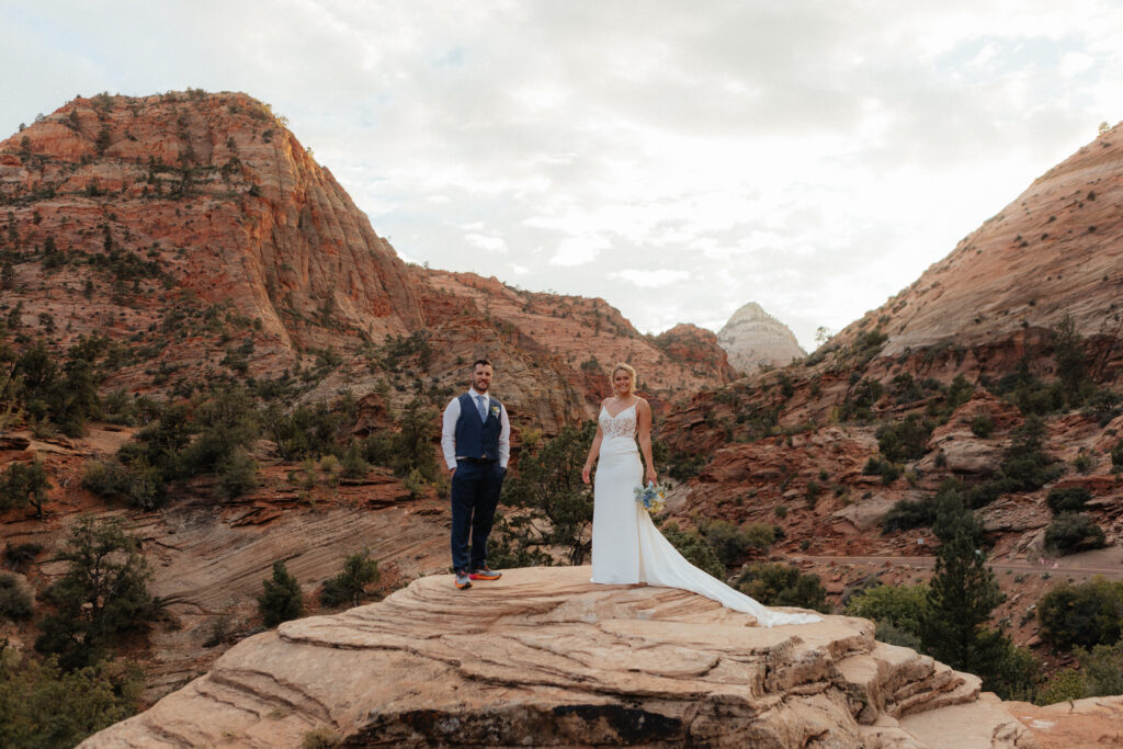 Bride and groom on a red rock ledge above the canyon at Canyon Overlook in Zion National Park