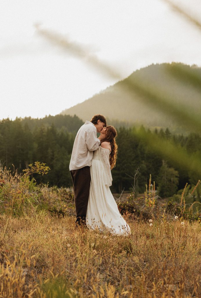 Dakota and Rowdy kissing in tall golden grass on a hillside framed by evergreens