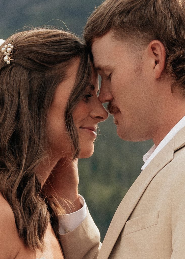 Bride and groom resting their foreheads together with Glacier's green mountains soft behind them