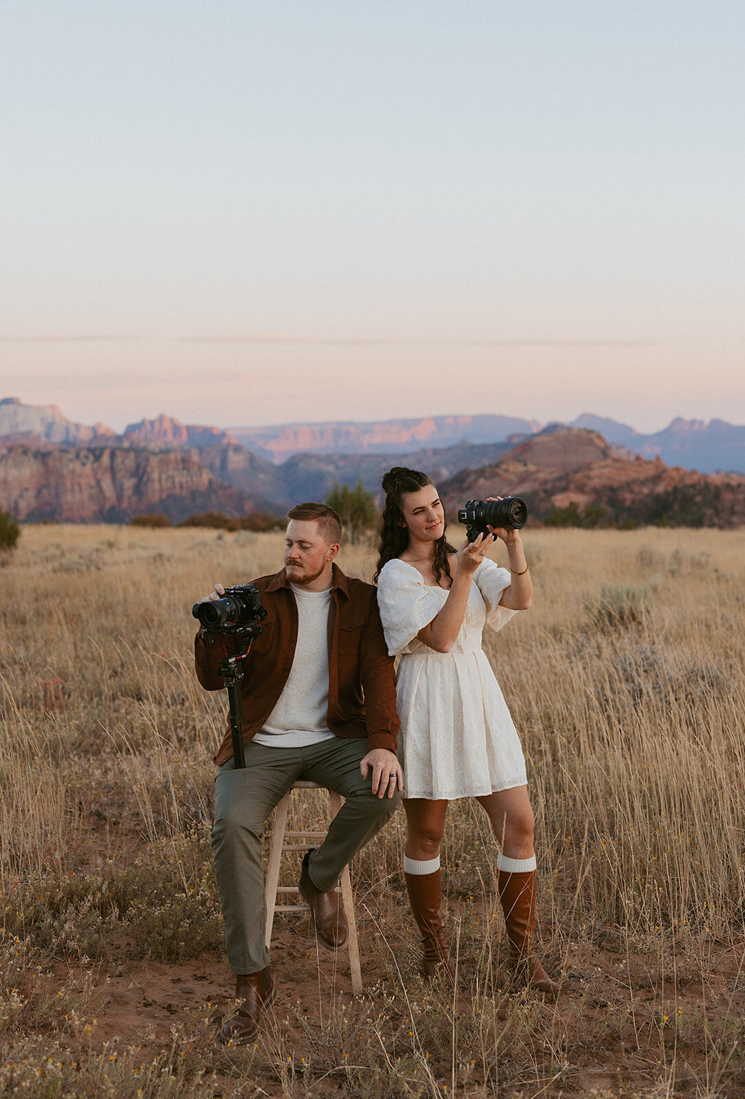 Sammie and Michael, a husband-and-wife photo and video team, holding their cameras in a desert field at sunset